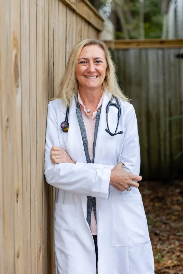 A woman in white lab coat standing next to wooden fence.